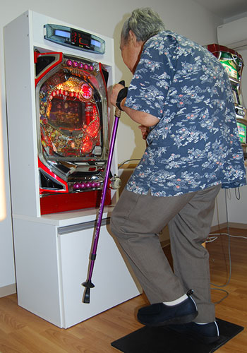 福祉施設で足踏みパッドを踏みながらパチンコを操作し、下肢の運動（機能訓練）として楽しむ様子